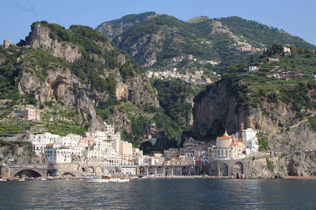 Pastel-coloured town of Atrani below steep green cliffs on the Amalfi Coast, Italy