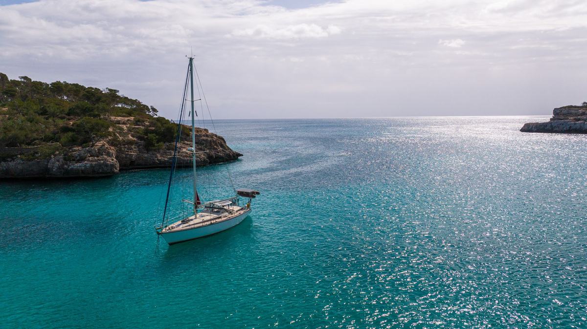 A white sailboat anchored in a turquoise cove on Mallorca